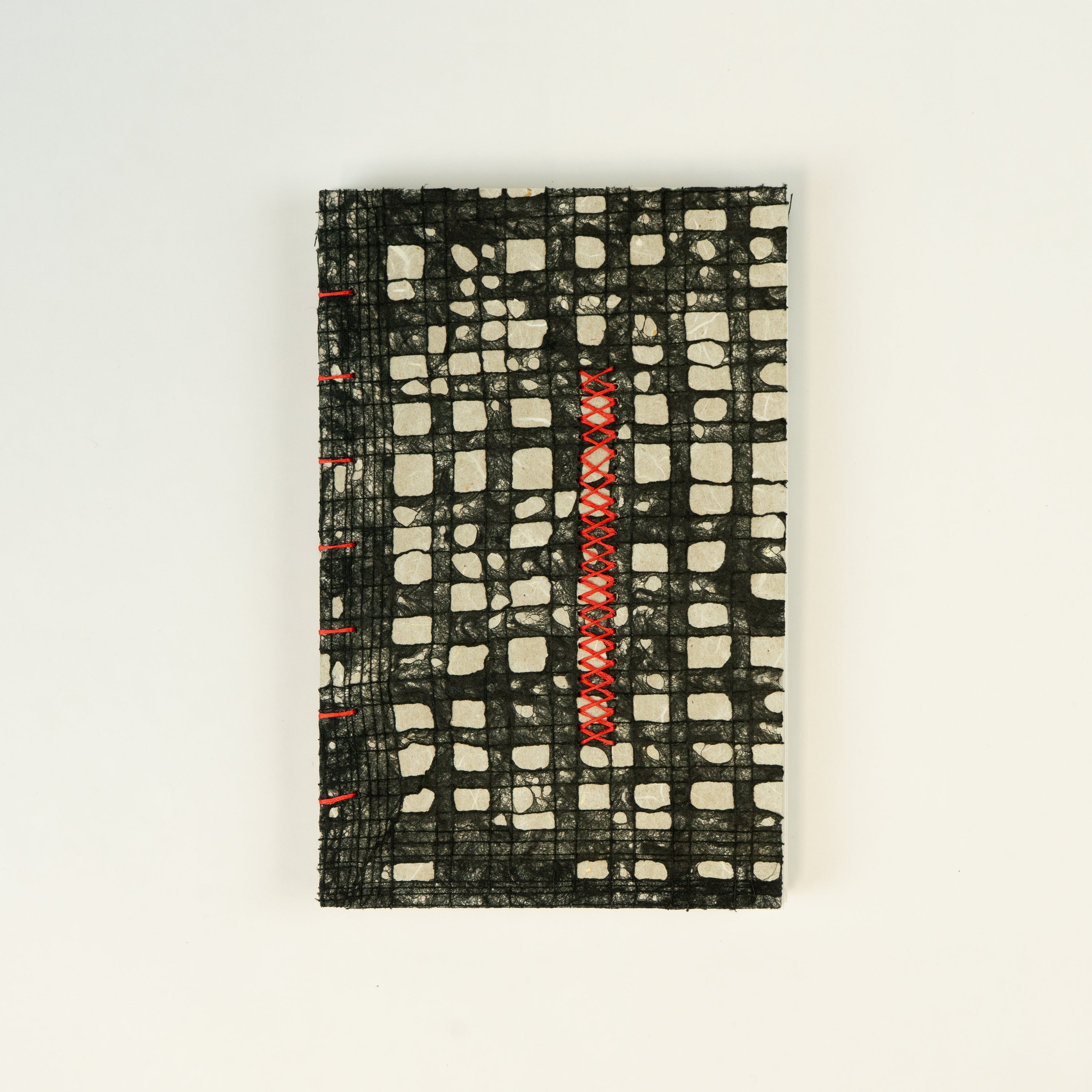 A hand-sewn book cover featuring a geometric pattern with a preponderance of black and gray tones, accented with red lines.