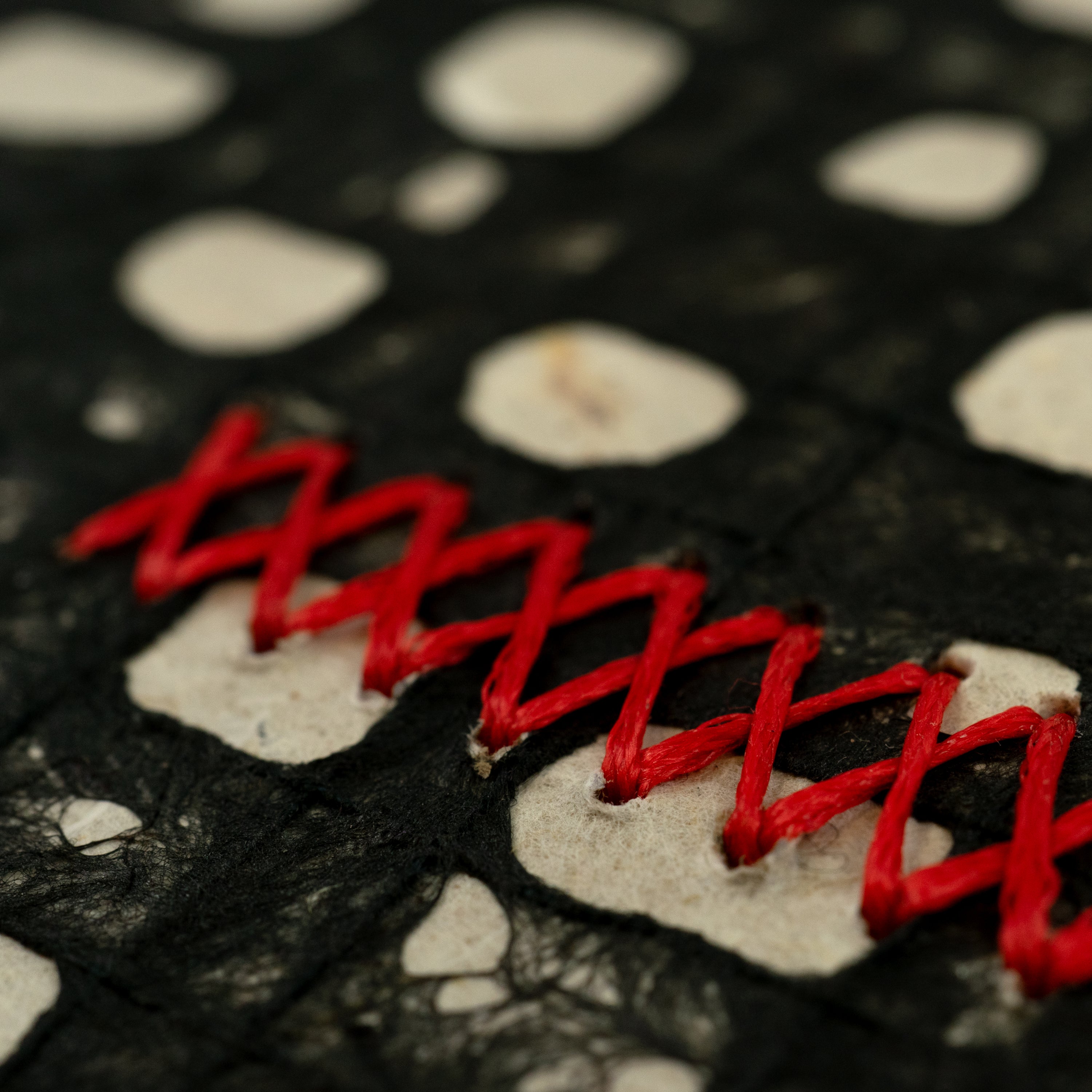 Close-up of a sewn red cross pattern on an abstract black-and-white surface.