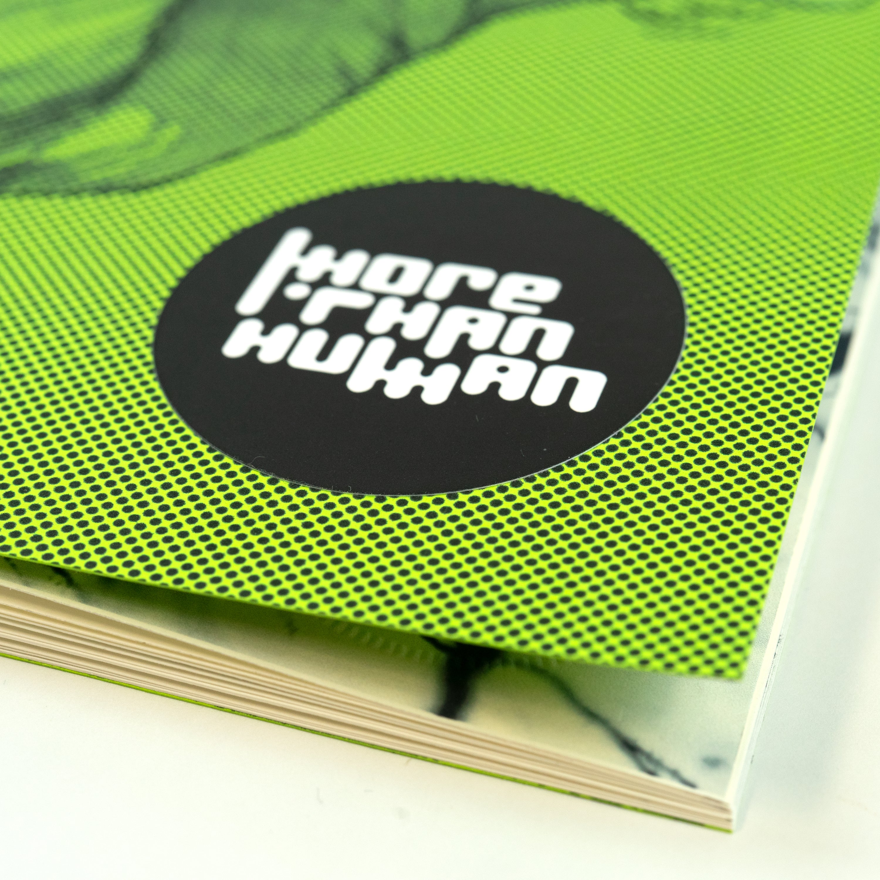 Close-up of a green zine corner with the title “More Than Human” on a black sticker with white letters.
