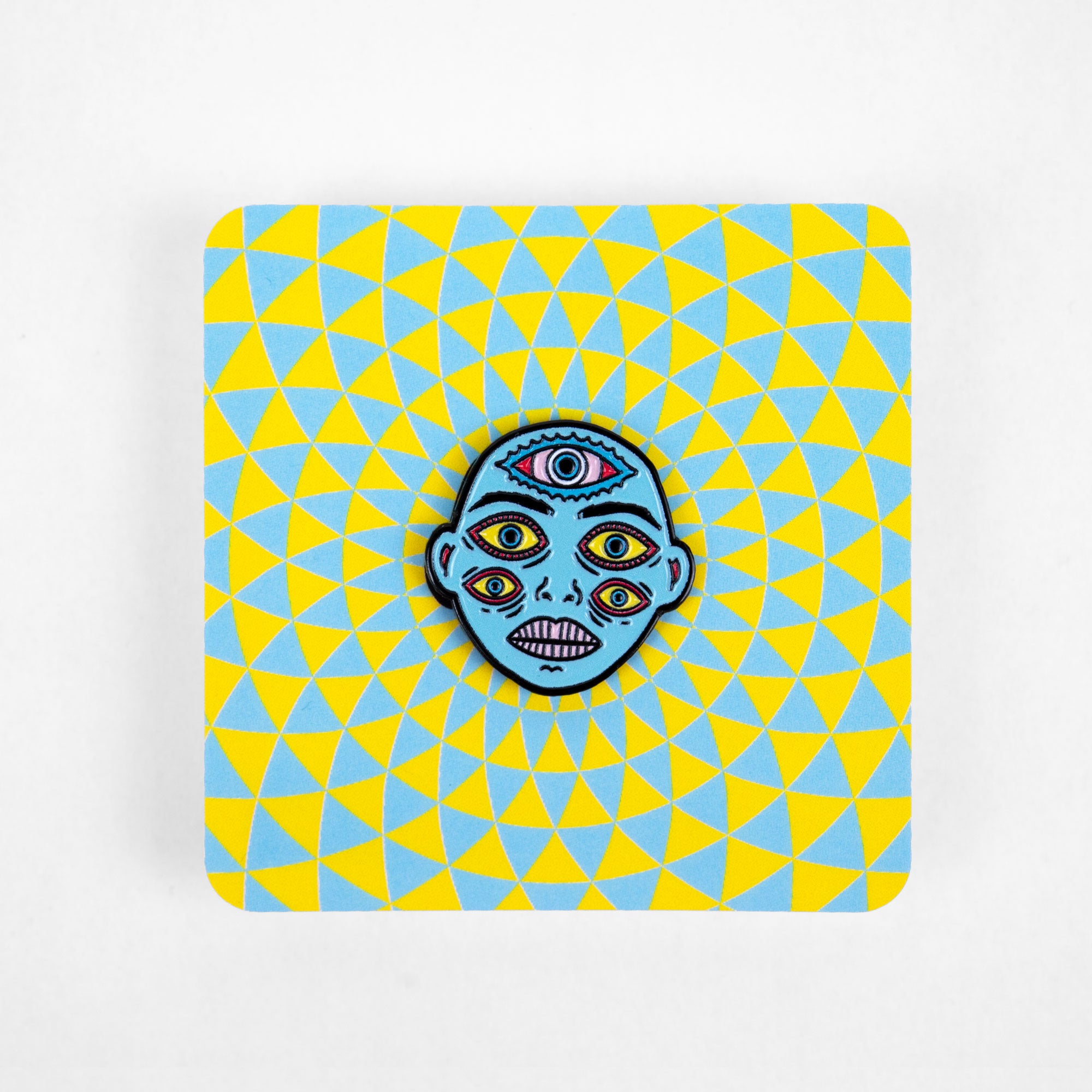 Enamel pin of a blue character attached to a square backing card with a yellow-and-blue pattern.